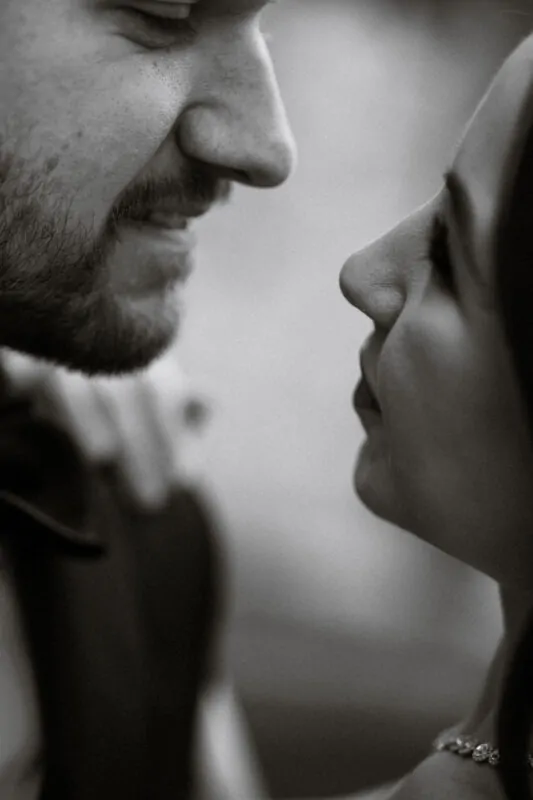 A close-up black and white portrait of a bride and groom standing nose to nose in a tender, intimate moment.
