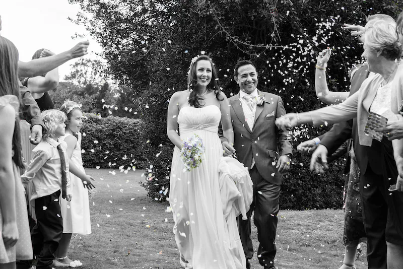 A newlywed couple walks through a shower of confetti tossed by joyful wedding guests outdoors.