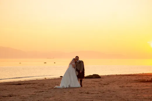 A newlywed couple poses together on a sandy beach during a breathtaking golden sunset over the calm sea.