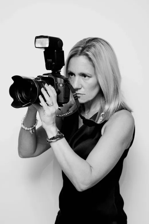 A blonde female wedding photographer focused intently through the viewfinder of her professional camera equipped with a speedlight flash.