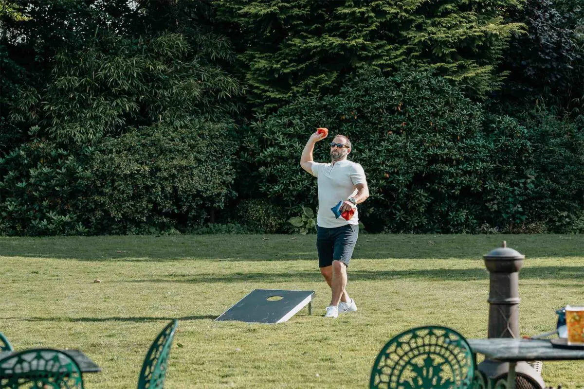 A guest enjoys playing lawn games on the grass during a sunny wedding reception in a garden setting.