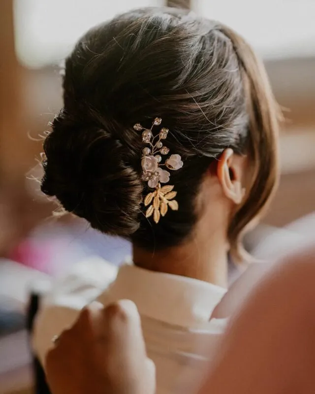 A close-up back view of a bride with a textured updo adorned with a delicate gold and floral hair comb during morning preparations.