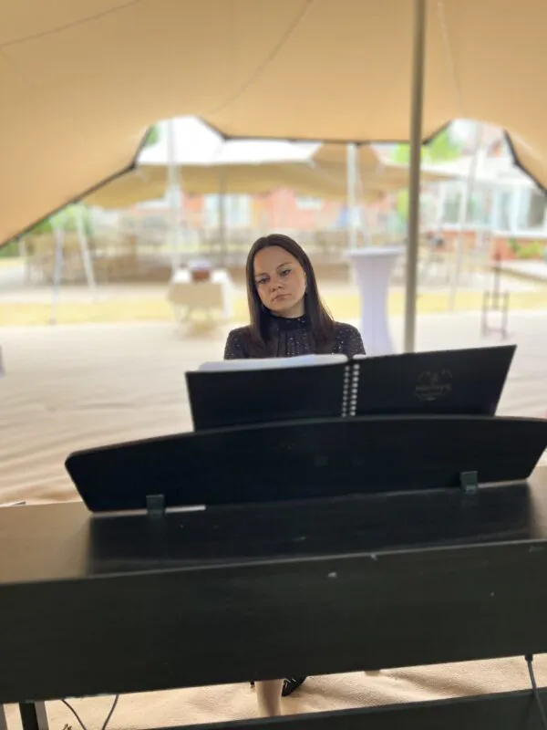 A female pianist focuses intently while playing a digital piano beneath a large marquee tent during a wedding reception.