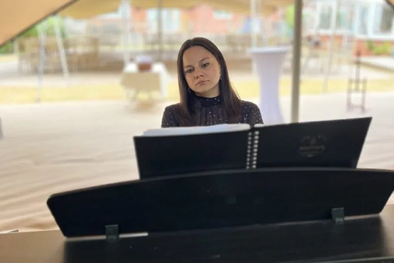 A female pianist focuses intently while playing a digital piano beneath a large marquee tent during a wedding reception.