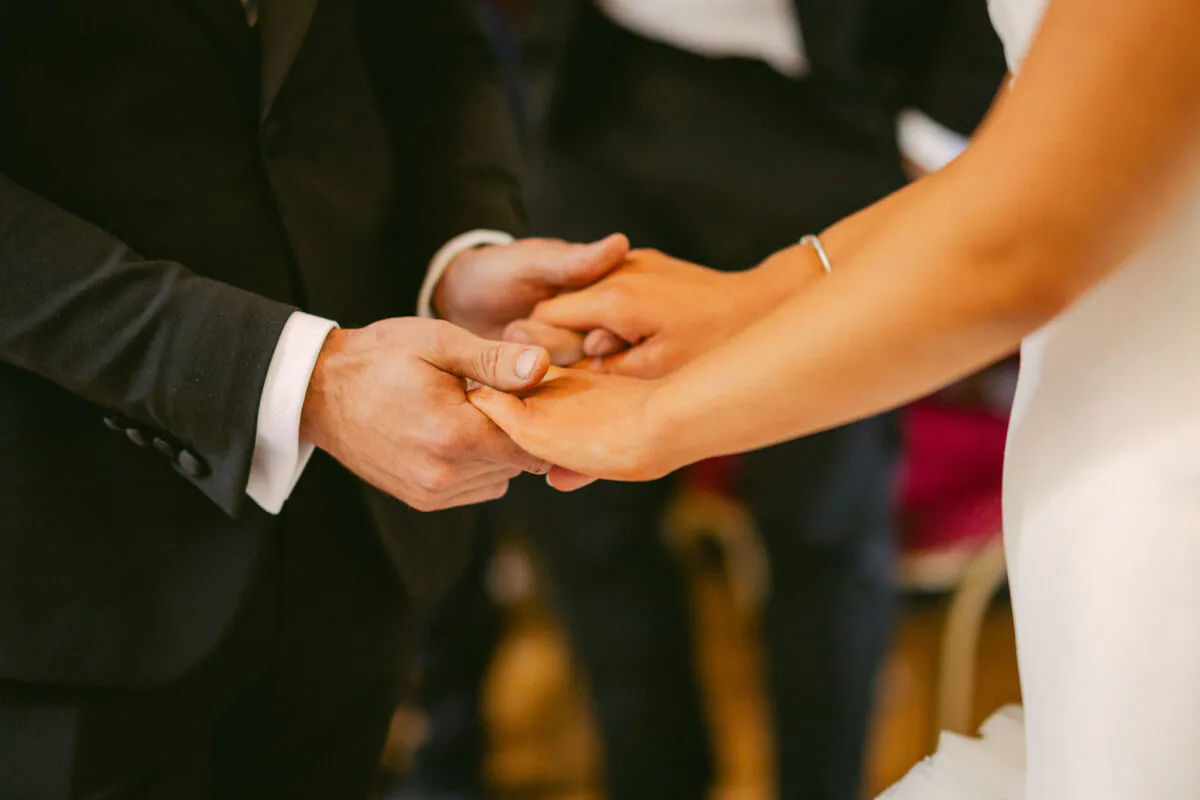 The bride and groom gently hold hands during their wedding ceremony, showcasing a tender and intimate moment.
