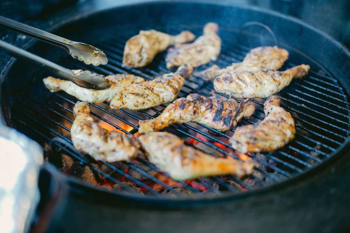 Several pieces of marinated chicken are grilling over hot coals on a barbecue at an outdoor wedding reception.