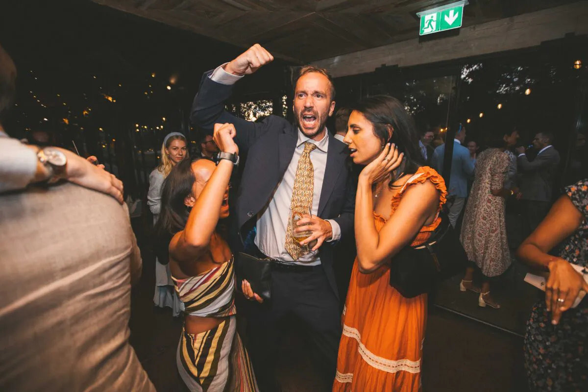 Guests celebrate on a lively illuminated dance floor with animated expressions and enthusiastic dancing during the evening wedding reception.