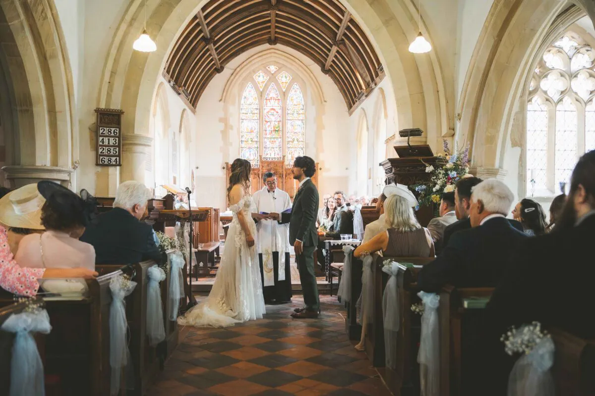 A bride and groom exchange rings during a traditional church ceremony inside a historic building with wooden pews and a vaulted timber ceiling.