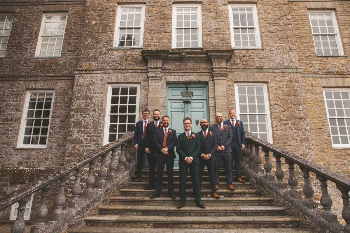 The groom and his groomsmen pose on the stone staircase outside a grand country house venue.
