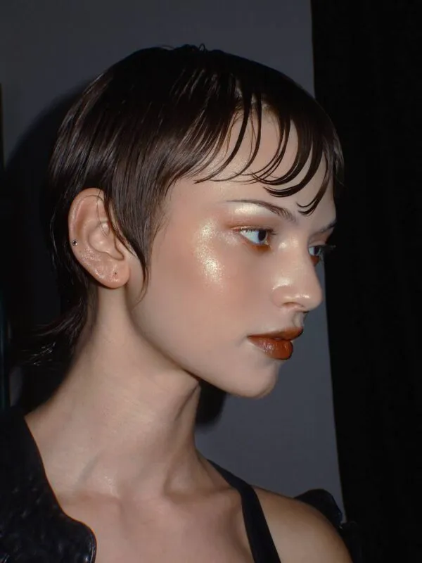 An extreme close-up editorial portrait of a bride featuring wet-look short hair, intensely highlighted skin, and a glossy lip captured with direct flash.