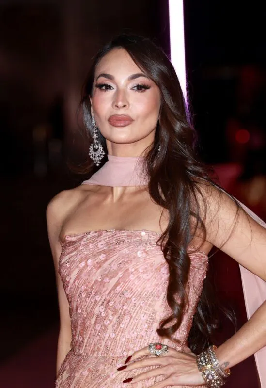 A close-up portrait of a bride featuring long wavy dark hair, a strapless blush pink sequin gown, statement drop earrings, and glamorous evening makeup.