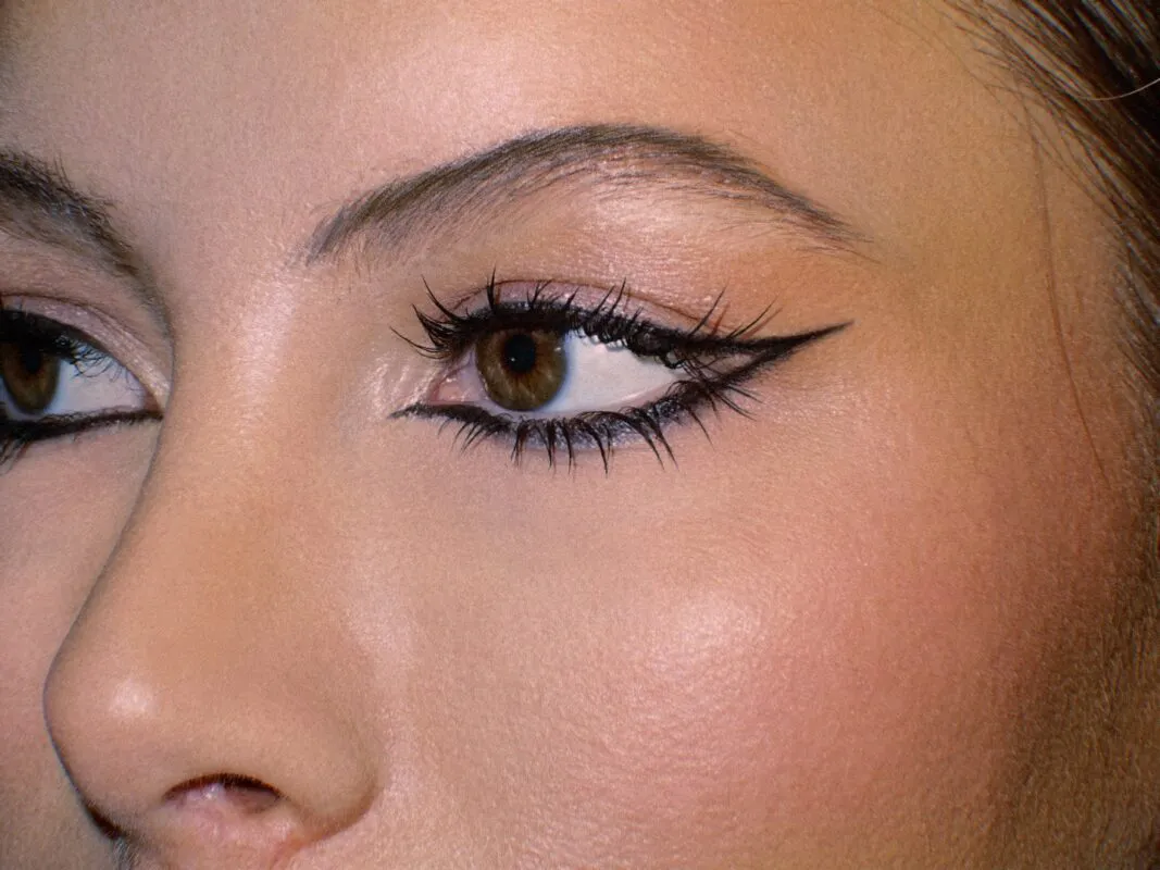 An extreme close up macro shot of a bride's face showcasing precise winged eyeliner, fluttery lashes, and neatly groomed brows with a warm editorial finish.