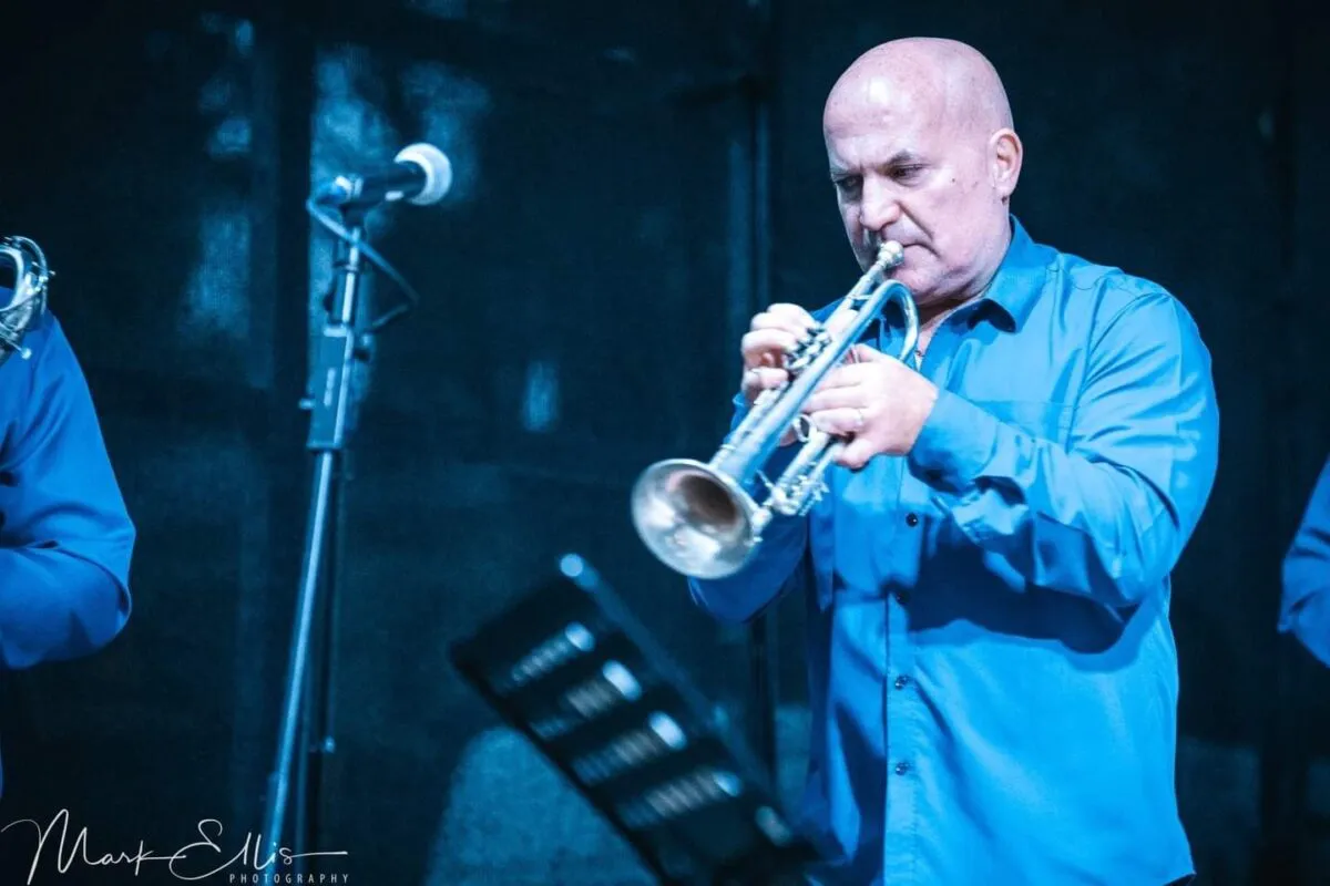 A musician wearing a blue shirt plays the trumpet on stage during an evening wedding reception performance.
