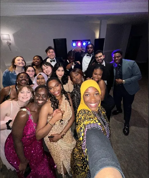 A joyful wedding crowd gathers close together for a group selfie on the dance floor under colourful disco lights.