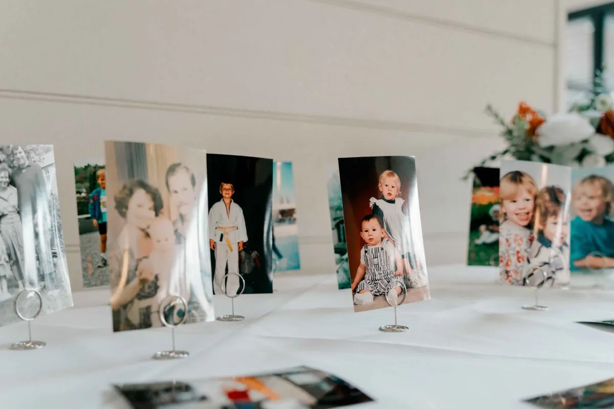 A thoughtful display of childhood photographs arranged in small wire holders on a white-covered table at a wedding celebration.