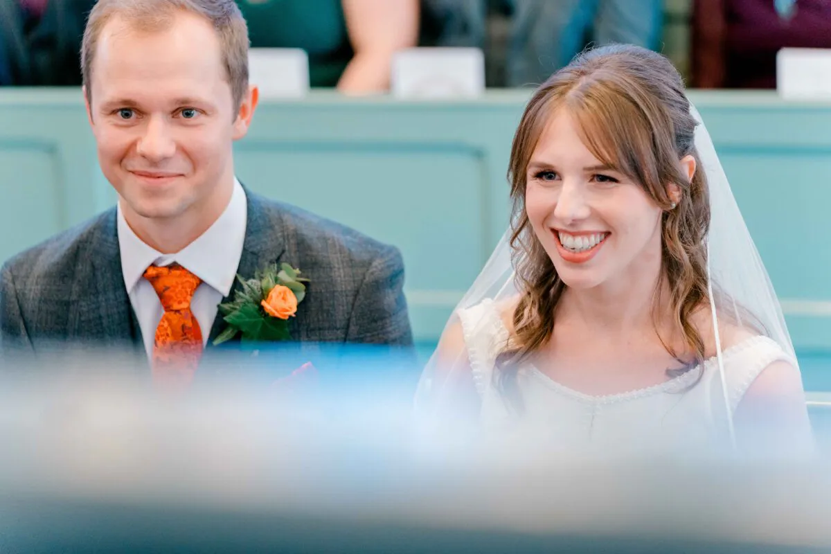 A smiling bride and groom sitting together during their church wedding ceremony, captured in candid natural light with traditional attire.