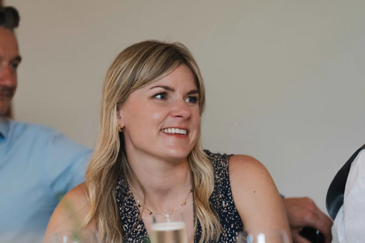 A blonde female wedding guest smiles candidly while seated at the reception dinner table among other guests.