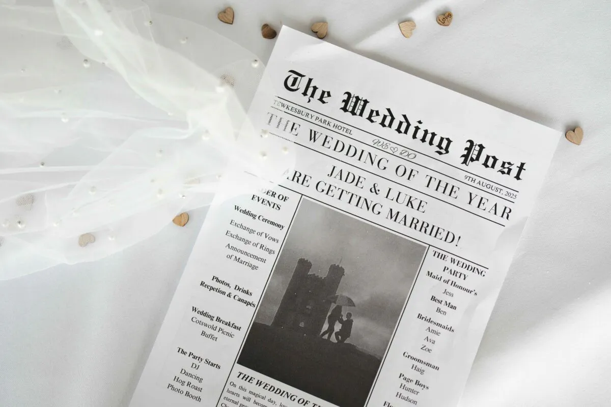 A bridal flat lay featuring a custom newspaper wedding stationery program alongside a delicate pearl-embellished veil on a white fabric background.