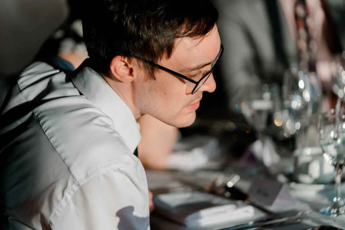 A wedding guest wearing glasses and a white shirt is captured in profile, focused intently during the wedding breakfast.