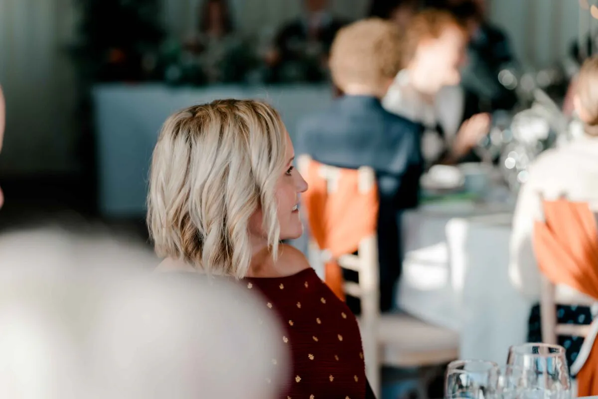 A blonde guest with a stylish bob haircut smiles while seated at a wedding reception banquet table.