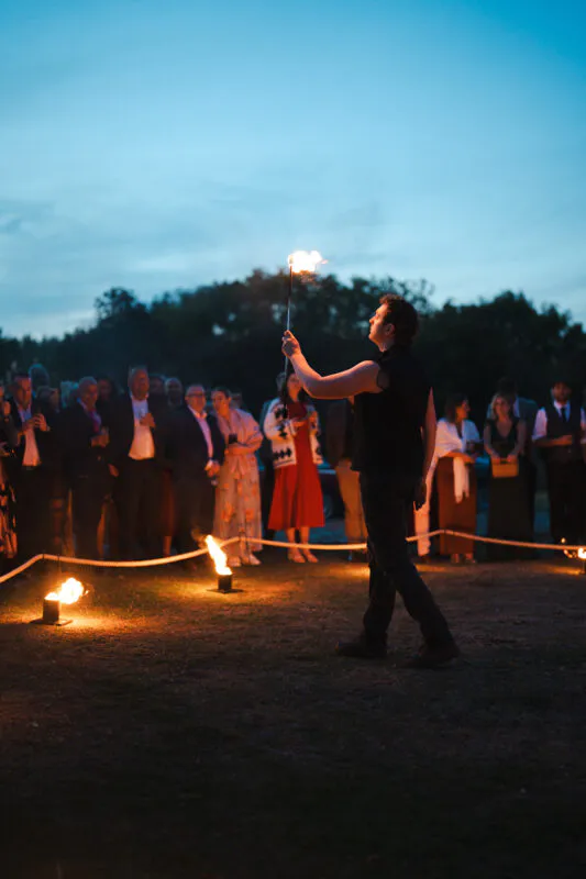 A fire performer entertains an outdoor evening crowd of wedding guests during the blue hour.