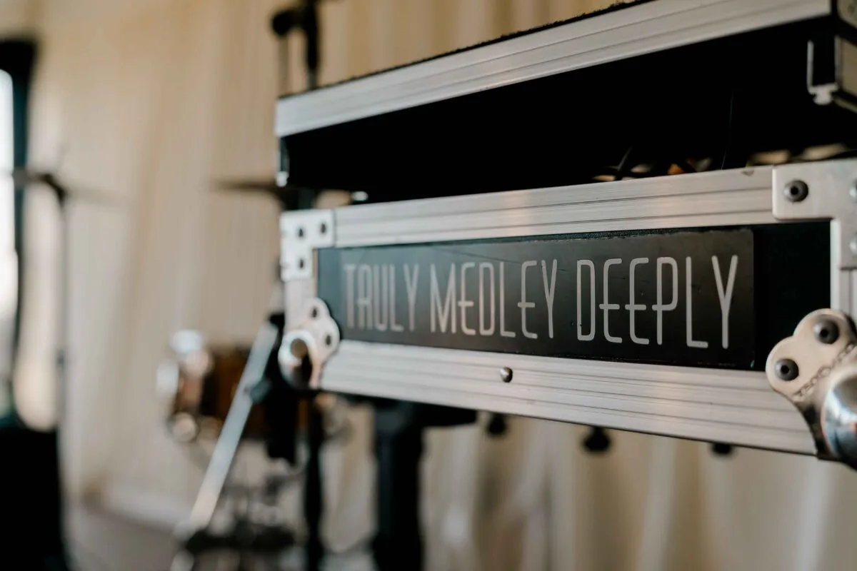 A close-up shot of a flight case with the words Truly Medley Deeply displayed on it, set against a softly blurred background of music equipment.