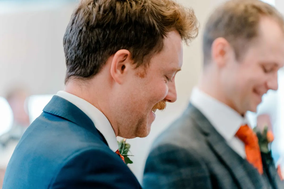 A close-up profile shot of a smiling groom in a blue suit with a boutonniere during the wedding ceremony.