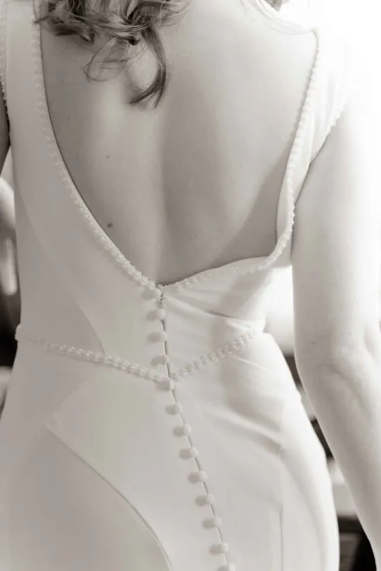 A close-up view of a bride's back in a low-cut gown featuring delicate pearl detailing and fabric-covered buttons down the spine.