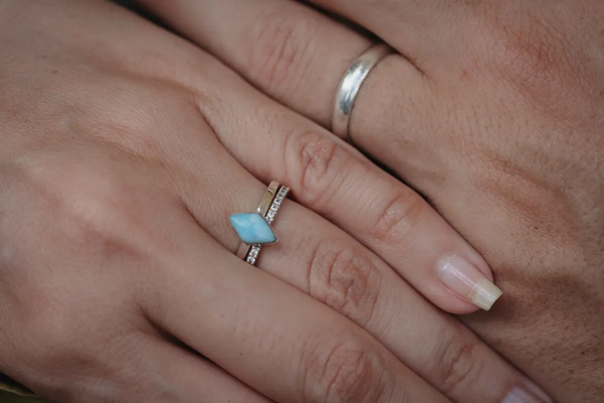 Close-up shot of hands gently touching, showcasing a distinctive turquoise engagement ring stacked with a delicate band next to a plain wedding ring.