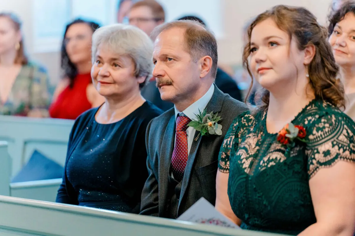 Family members and guests seated in a church pew during a wedding ceremony, watching attentively.