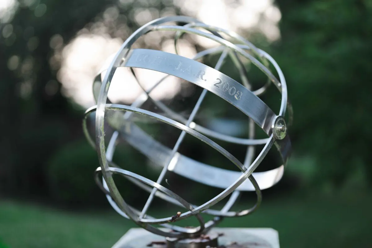 A close-up shot of an engraved metallic armillary sphere sculpture outdoors with a softly blurred garden background.