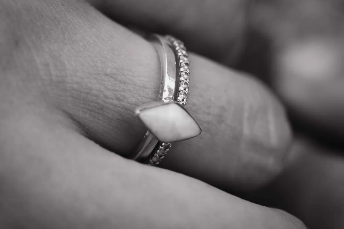 An extreme close-up black and white shot captures stacked wedding rings and a distinctive diamond-shaped gemstone resting on a finger.