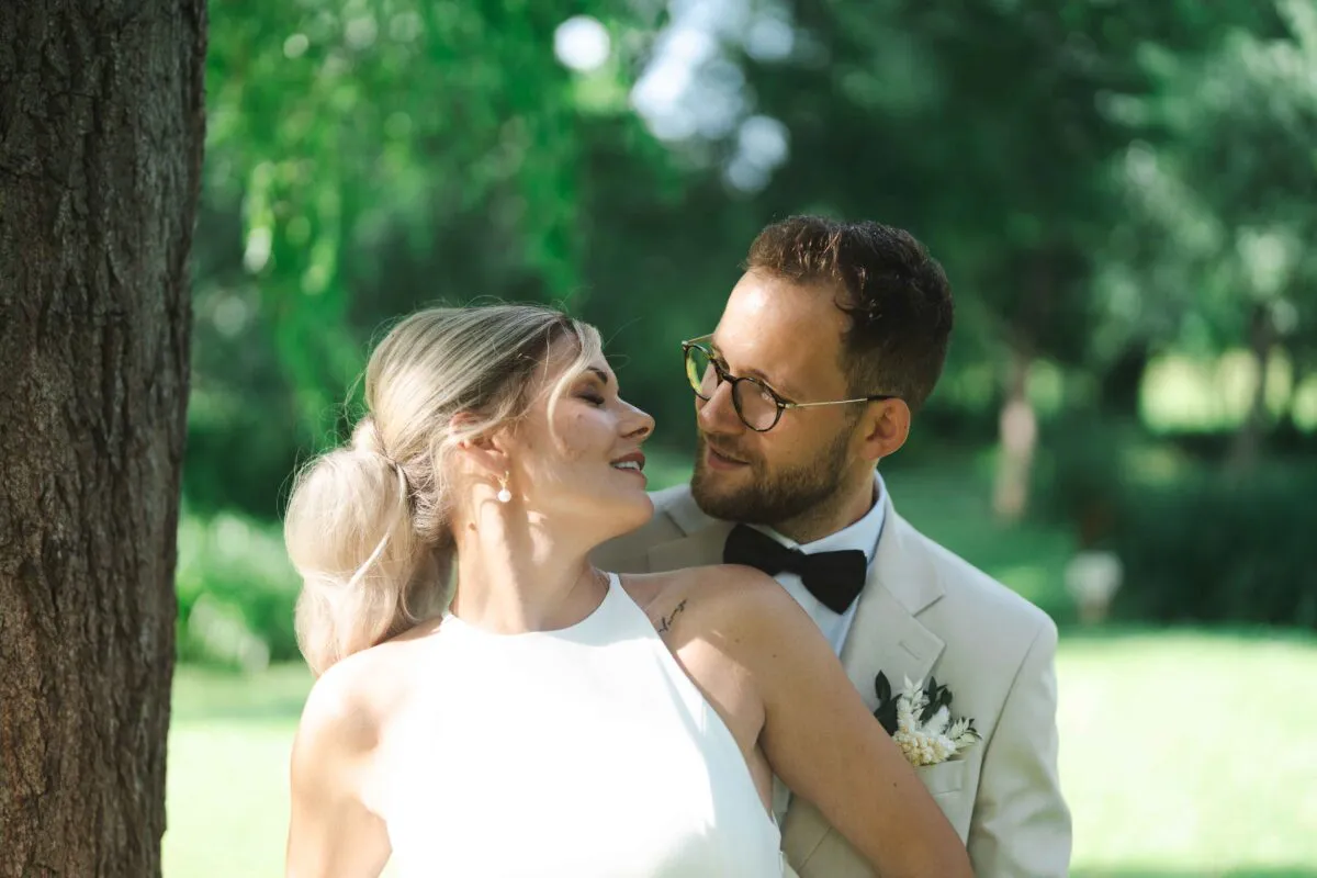 A newlywed couple share a tender glance amidst a sunlit woodland backdrop during their outdoor wedding portrait session.