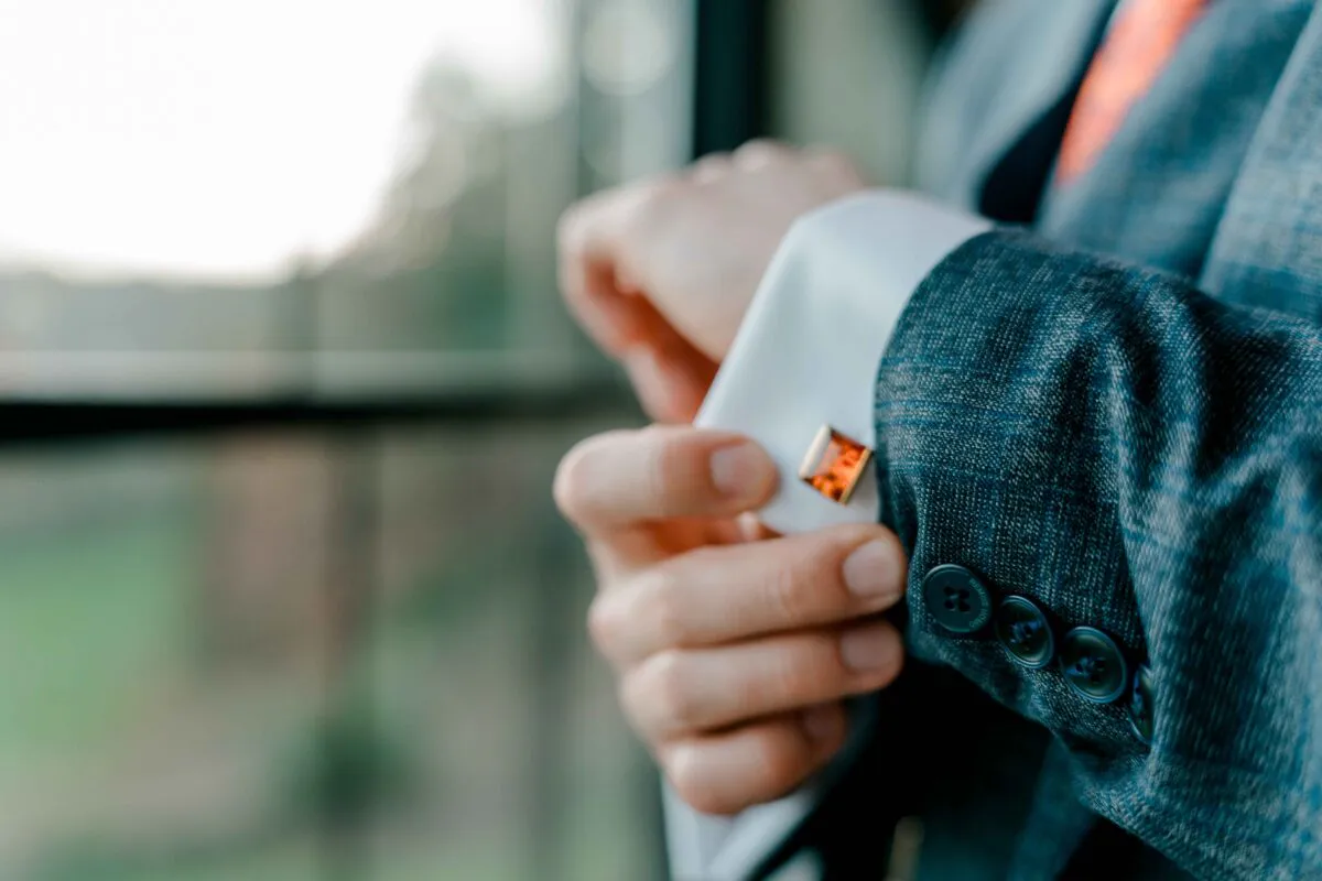 A close-up shot of a groom fastening his cufflinks while getting ready for the wedding near a window.
