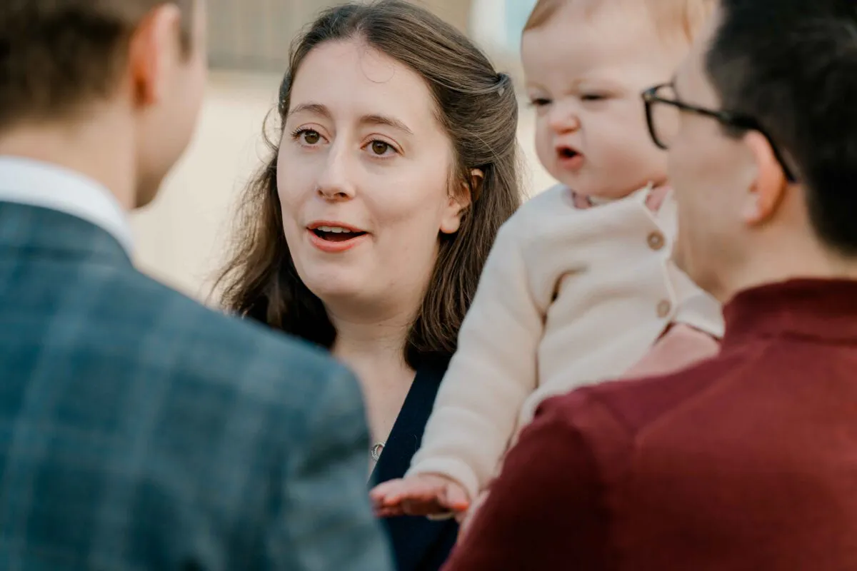 A woman holding a baby engages in conversation with family members during a relaxed wedding guest mingling moment.