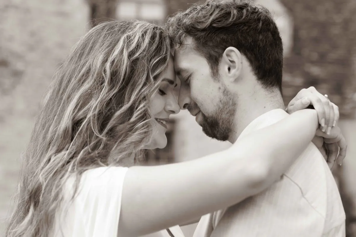 A newlywed couple embraces tenderly with their foreheads touching in a warm sepia toned portrait.