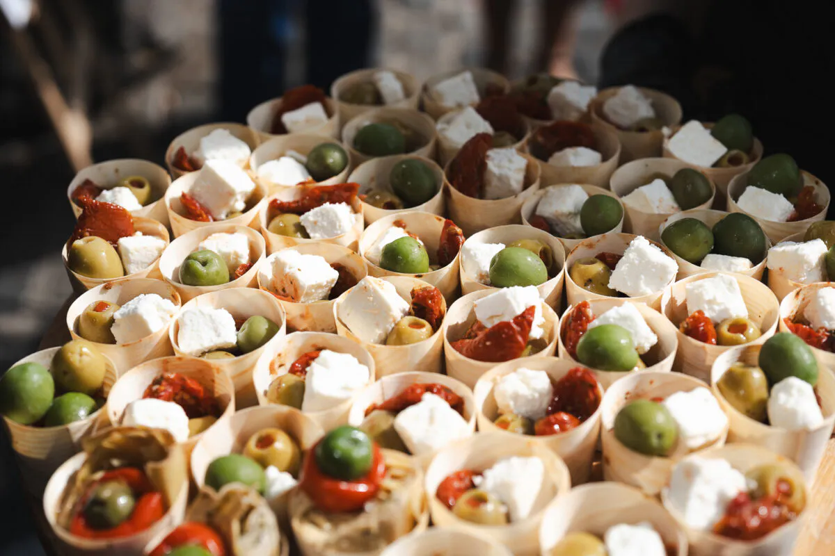 A close-up high-angle shot of numerous individual canape cups filled with green olives, feta cheese, and sun-dried tomatoes.