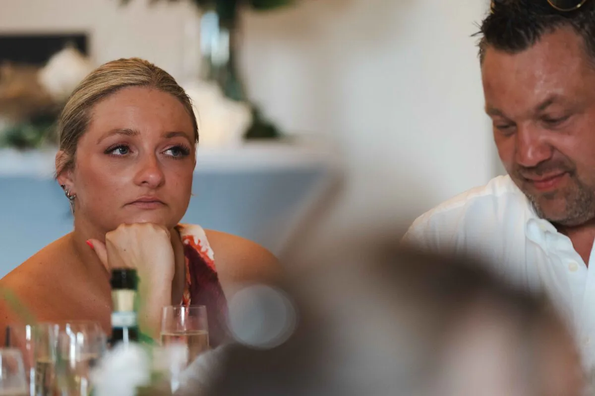 An emotional wedding guest rests her chin on her hand while listening intently to speeches during the wedding breakfast.