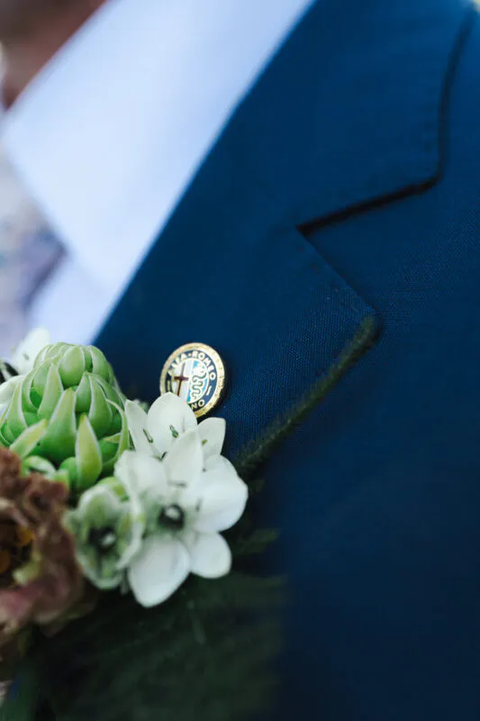 Close-up of a groom wearing a navy suit adorned with a textured floral buttonhole featuring white blooms and succulents.