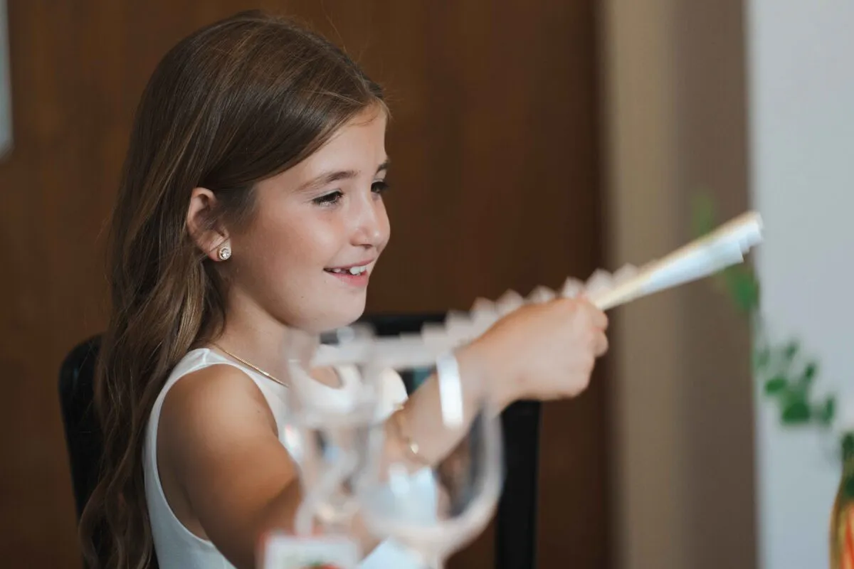 A young flower girl smiles happily while holding a decorative party favour during the wedding reception.