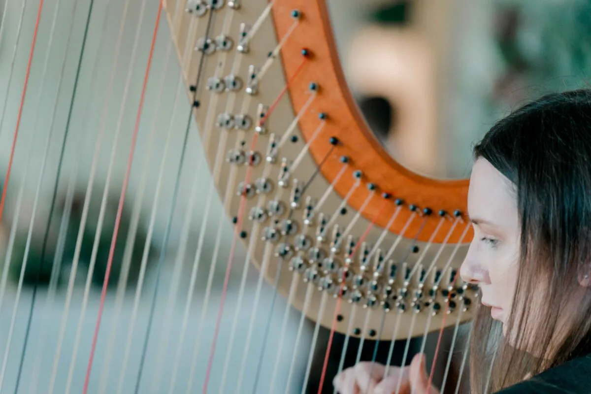 A close-up shot captures a musician gracefully playing a wooden harp, with her fingers gently plucking the strings during a wedding ceremony.