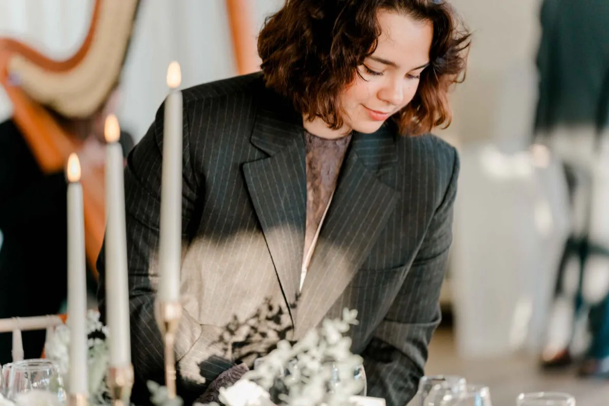 A person in a charcoal pinstripe blazer looks down thoughtfully near a table adorned with lit taper candles.