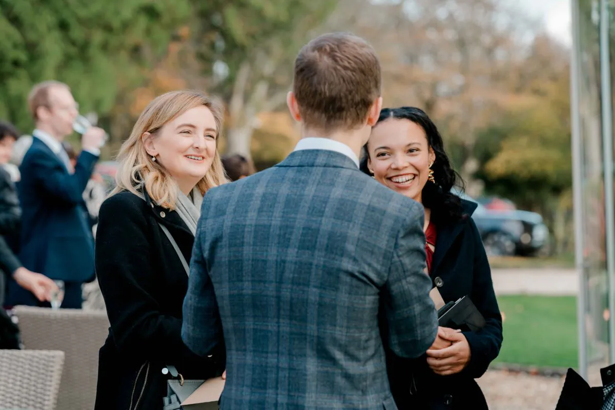 Wedding guests are captured mingling and laughing together outdoors during a drinks reception.
