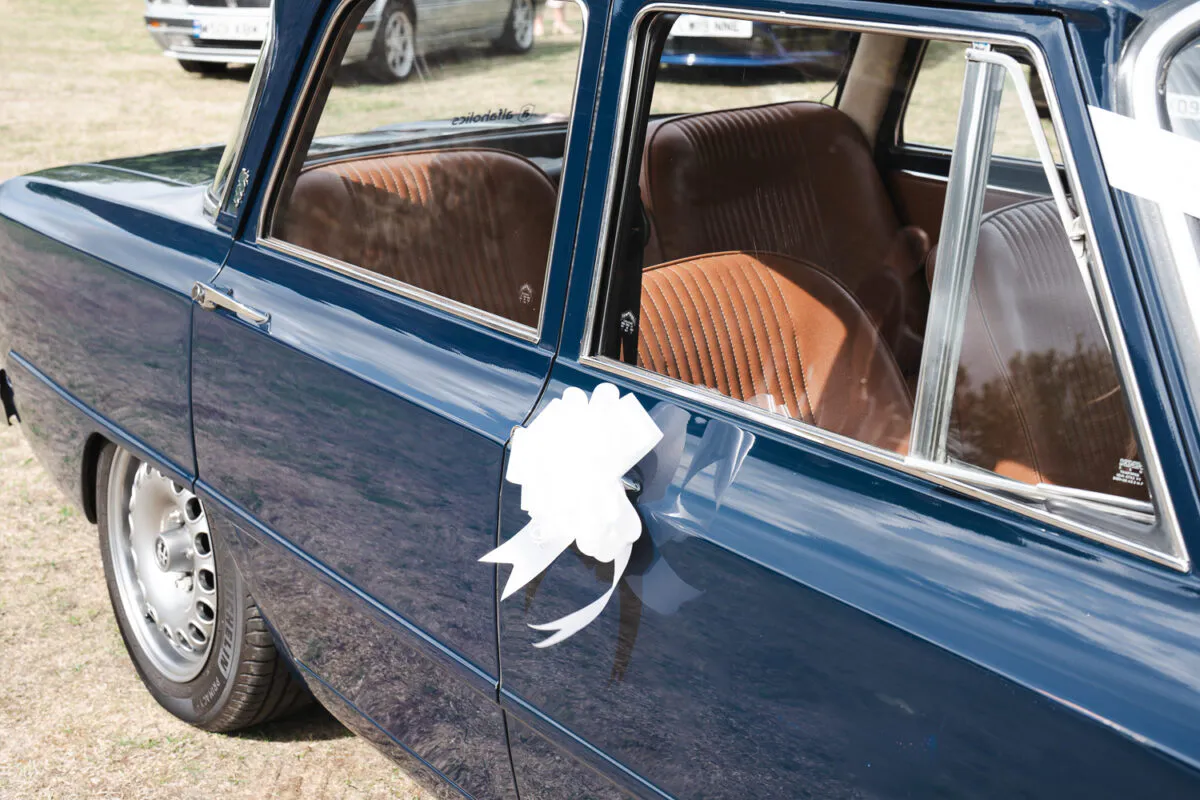 A classic dark blue wedding car decorated with a white ribbon on the door handle, showcasing its polished exterior and brown leather interior.