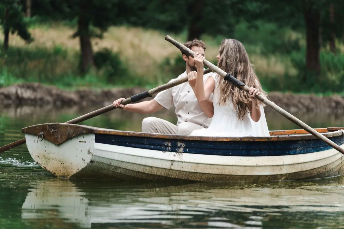 A bride and groom enjoy a romantic boat ride together on a calm lake, surrounded by lush green trees.