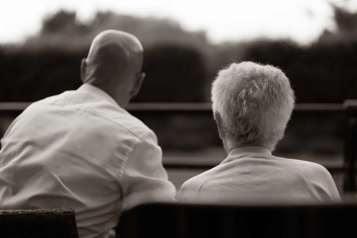 An emotional black and white shot from behind of an older couple sitting together quietly and looking outwards at a wedding.
