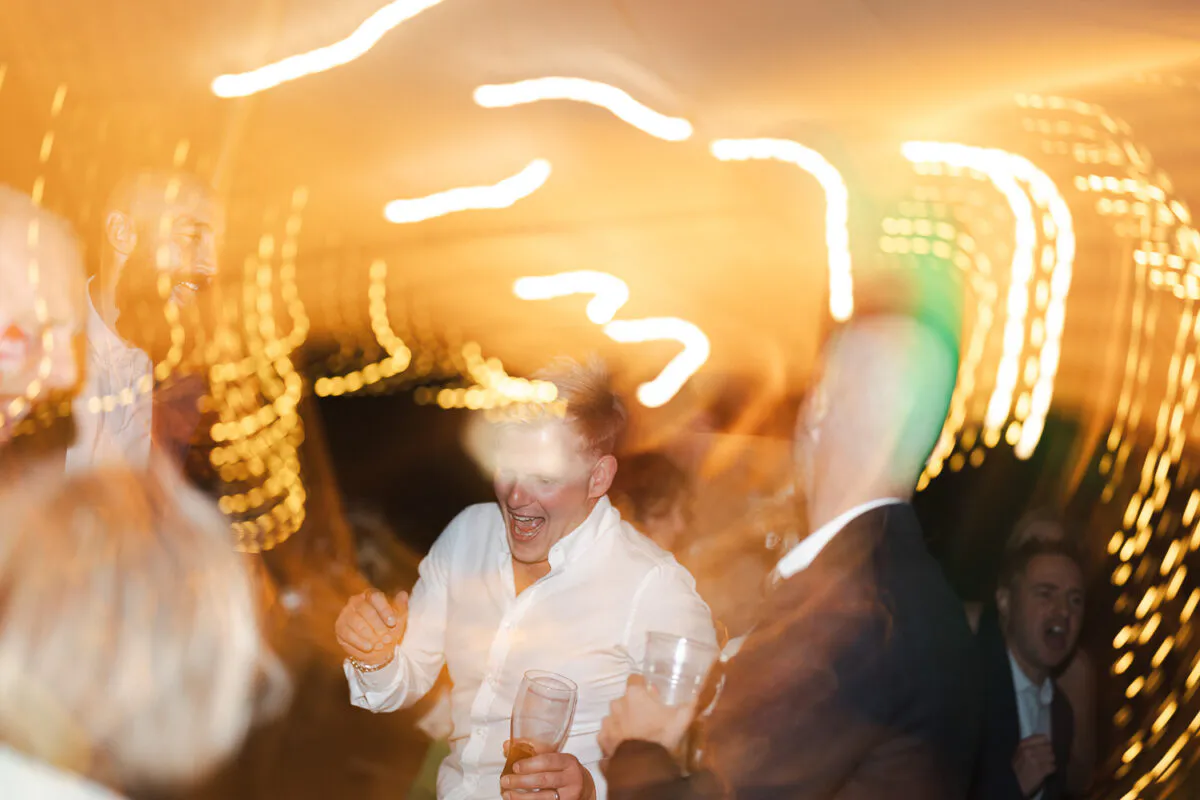 Wedding guests enjoy a lively moment on the dance floor under glowing lights, captured with dynamic motion blur.