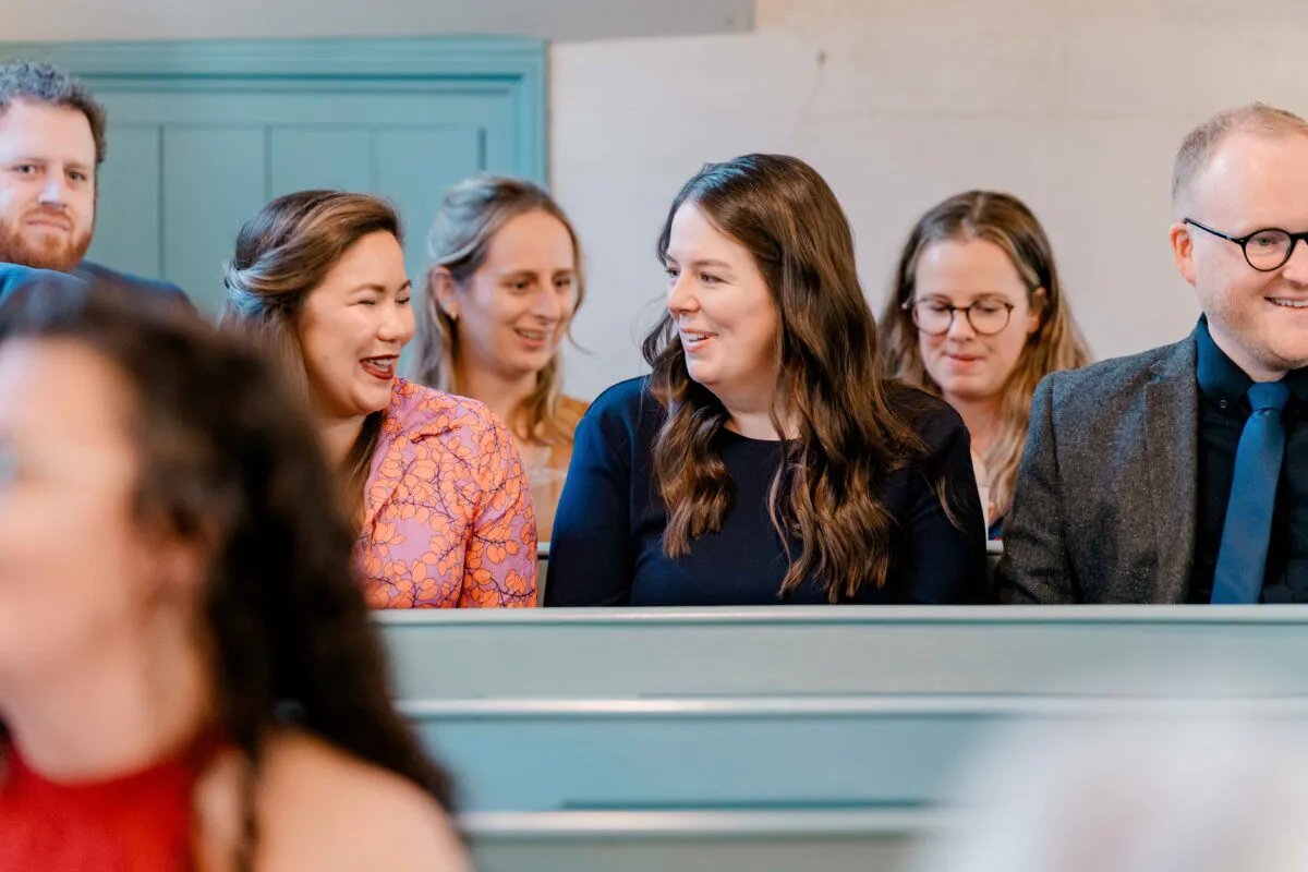 Wedding guests seated in church pews share a joyful moment of laughter during the ceremony.