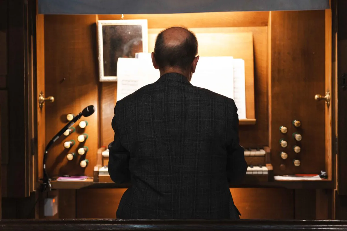 An organist seen from behind plays a large wooden pipe organ inside a church during a wedding ceremony.