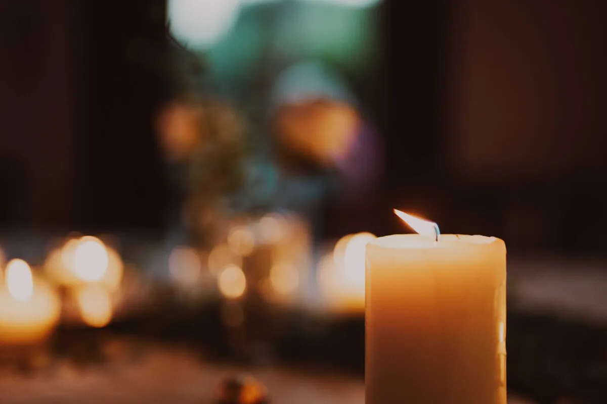 A close-up shot of a single lit pillar candle in the foreground, with a soft-focus background filled with warm bokeh lights and romantic candlelight.